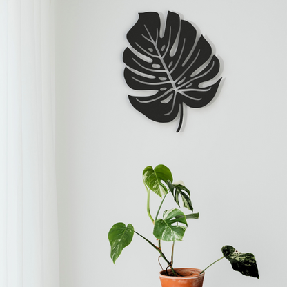 black monstera leaf metal wall art on wall above a plant